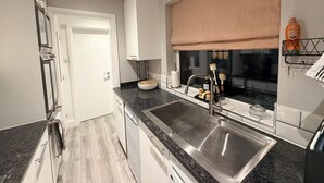 A modern kitchen with a double sink, stainless steel appliances, and a window with a beige blind. - 3 bed, 'Adrian Cottage' close to Warner Bros, M25, M1. Comes with private gym (Abbots Langley)