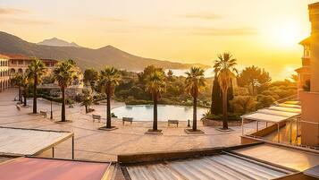 A rooftop terrace with a view of a beach and mountains during sunset.