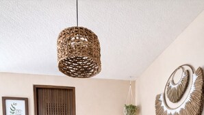 Ein Essbereich mit einem runden Tisch, vier Holzstühlen, einer hängenden Lampenschirm aus Bändern, einer Holztür und einem Wandbild.