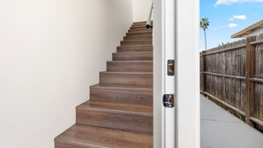 A wooden staircase leading to a white door, a wooden fence, and a palm tree in the background. - Light-Filled ADU Studio • Immaculate, Cozy & Convenient (San Diego)