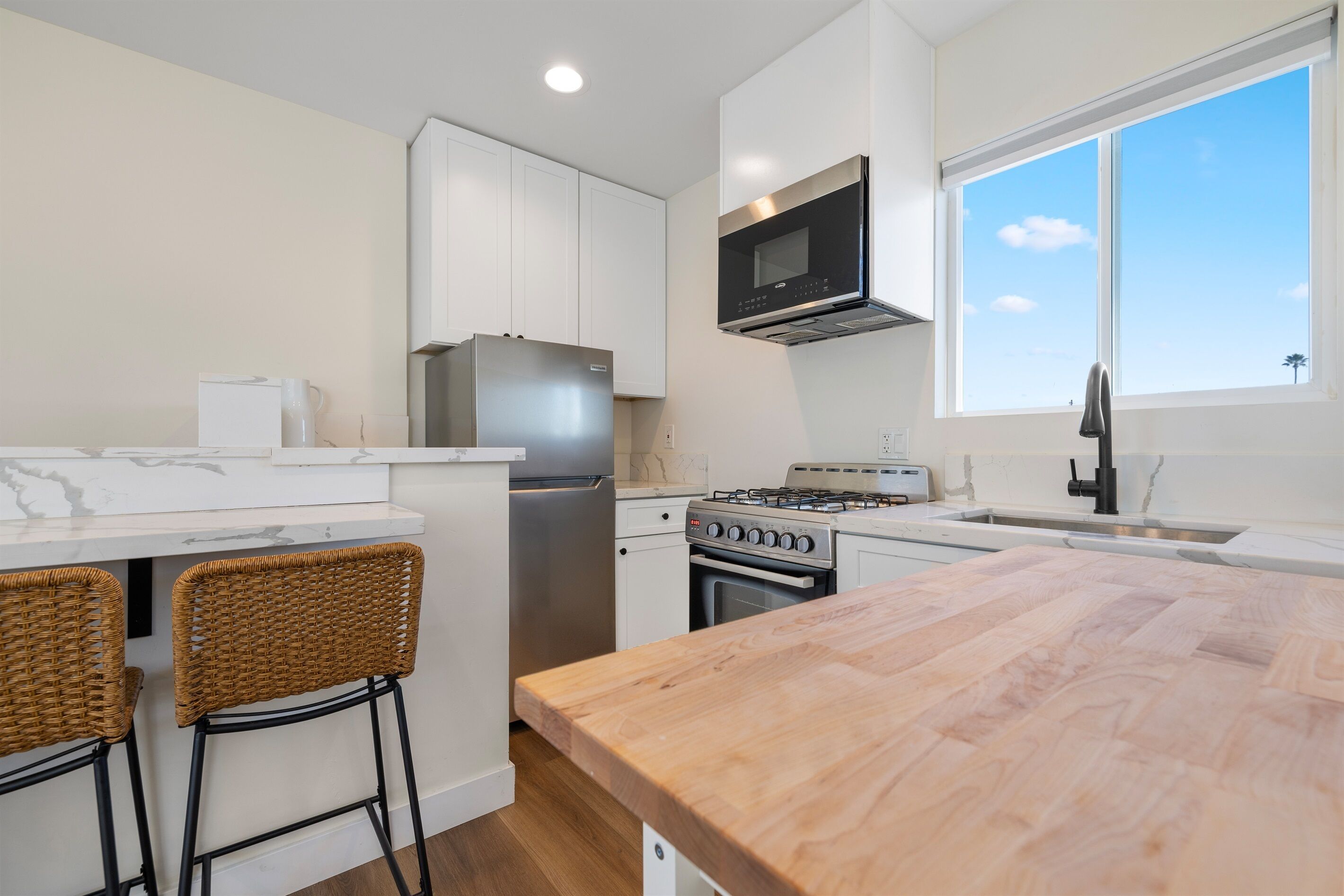 A modern kitchen with white cabinets, stainless steel appliances, a wooden island, and a large window.