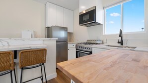 A modern kitchen with white cabinets, stainless steel appliances, a wooden island, and a large window. - Light-Filled ADU Studio • Immaculate, Cozy & Convenient (San Diego)