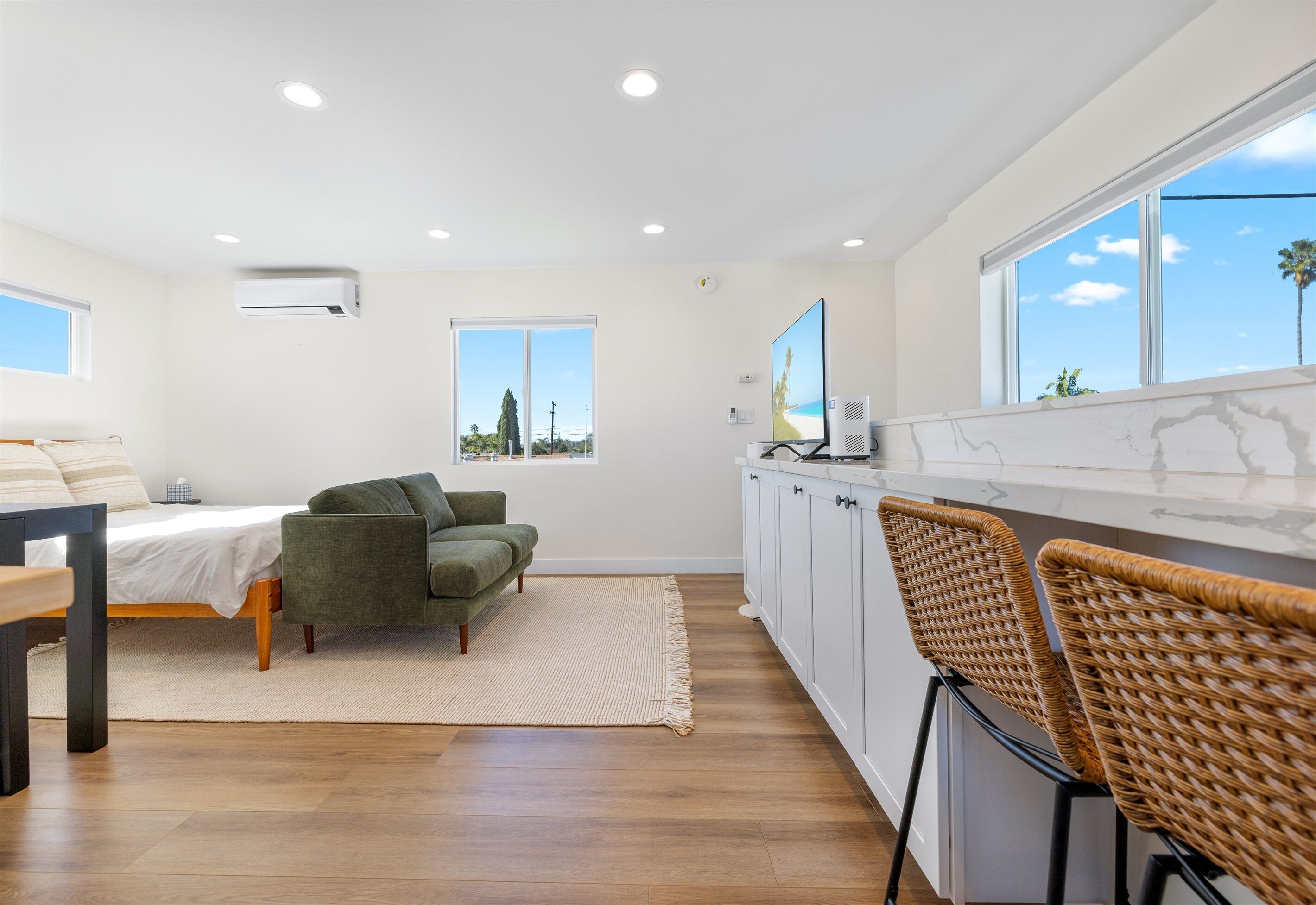 A modern kitchen with white cabinets, a dining area with a table and chairs, and a large window with a view of trees.