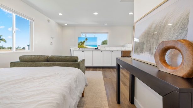A bedroom with a bed, a sofa, a desk with a painting, and a view of the ocean through a window. - Light-Filled ADU Studio • Immaculate, Cozy & Convenient (San Diego)