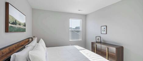 Un dormitorio con cama, cómoda, ventana con persianas y luz en el techo.