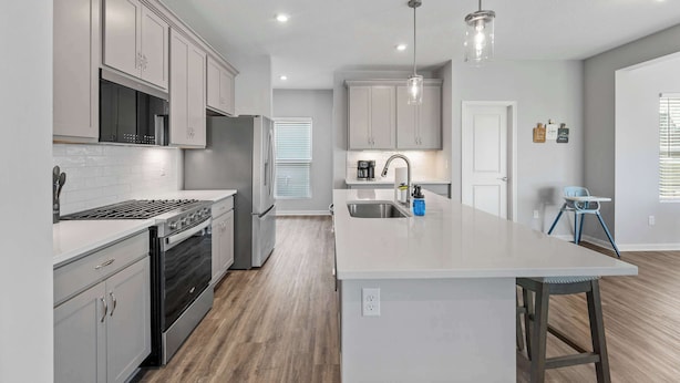 A modern kitchen with grey cabinets, a central island, stainless steel appliances, and pendant lighting. - Ark & Creation Stay New Home (Walton)