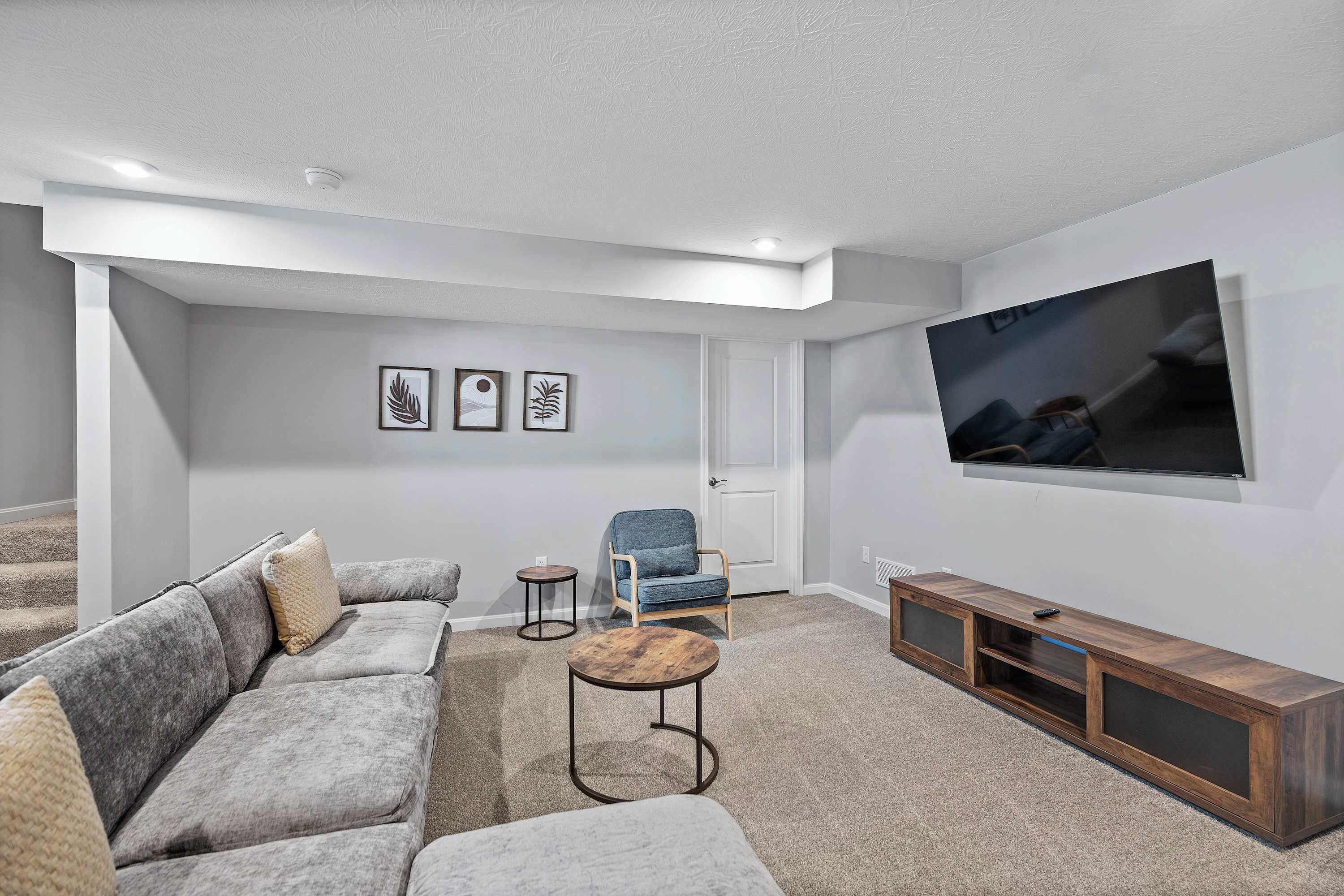 A modern living room with a grey sectional sofa, a blue armchair, a wooden coffee table, and a TV on a wooden stand.