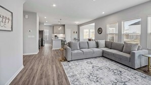 A modern living room with a grey sectional sofa, a patterned rug, and a kitchen in the background. - Ark & Creation Stay New Home (Walton)