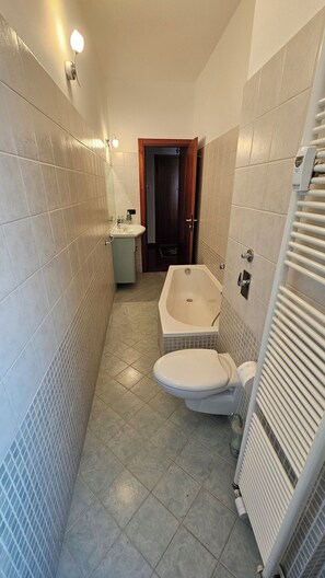 Ein schmales Badezimmer mit Badewanne, Toilette und Waschbecken.