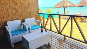Un pontile in legno con mobili in vimini, un ombrellone di paglia e vista sulla spiaggia.