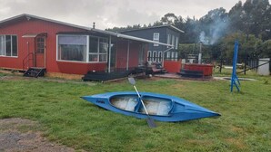 Una casa roja con porche cubierto y un canoa azul sobre el césped.