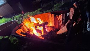Una fogata en un brasero metálico, con leños y una mesa metálica cerca.