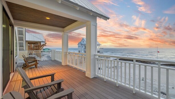 A wooden deck with a railing, overlooking a beach with a sunset. - NEW! Lux Beachfront, Views, Heated Pool, Sleeps 24 (Panama City Beach)