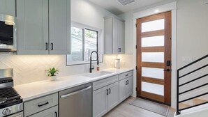 Une cuisine moderne avec des meubles de couleur gris clair, une hotte de cuisine en acier inoxydable, un évier avec un robinet noir et une porte à cadre en bois.