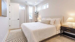 Une chambre à coucher avec un grand lit, des lampes de chevet, une table de nuit, une fenêtre avec des rideaux et un ventilateur de plafond.