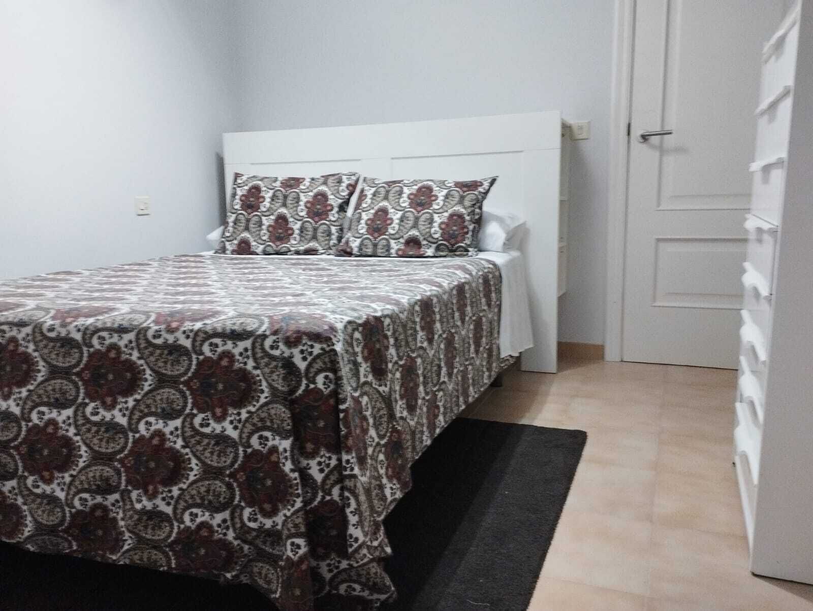 A small, neatly arranged bedroom with a bed, a bedside table, and a wardrobe.