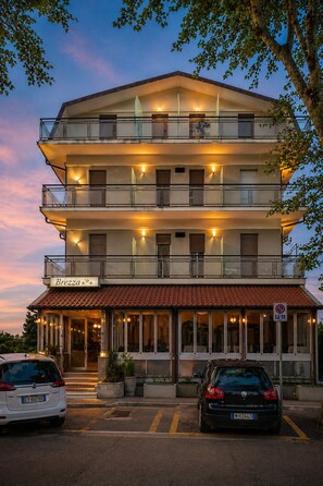 A multi-story hotel with balconies, a sign reading 'Brezza,' and a parking area with cars. - Hotel Brezza (Rimini)