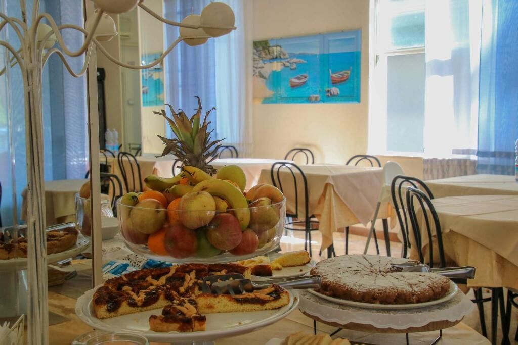 A dining area with a fruit bowl, a cake, and a pizza on a table.