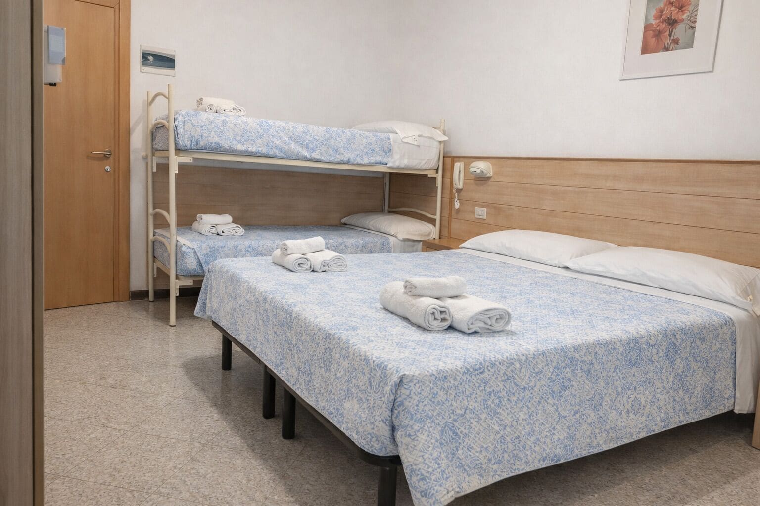 A room with two bunk beds, a wooden door, a small bedside table with a phone, and a wall-mounted picture.