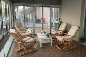 A room with wicker rocking chairs, a small white table, and a glass door leading outside. - Hotel Brezza (Rimini)