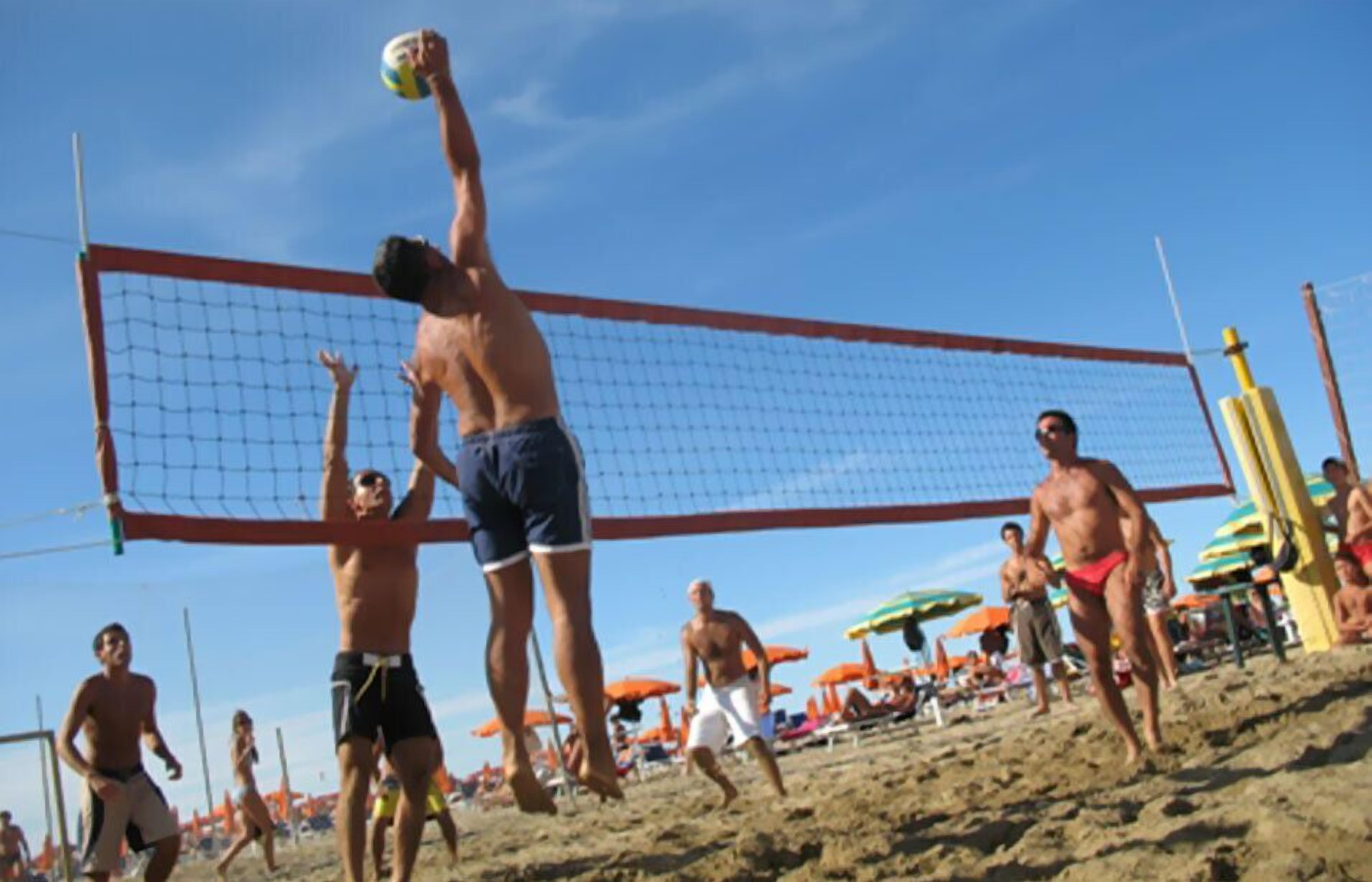 A beach volleyball game with players in swimwear, a net, and beach umbrellas in the background.