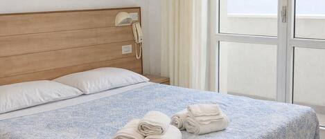 A neatly made bed with a patterned bedspread, a wooden headboard, and a telephone on the wall.