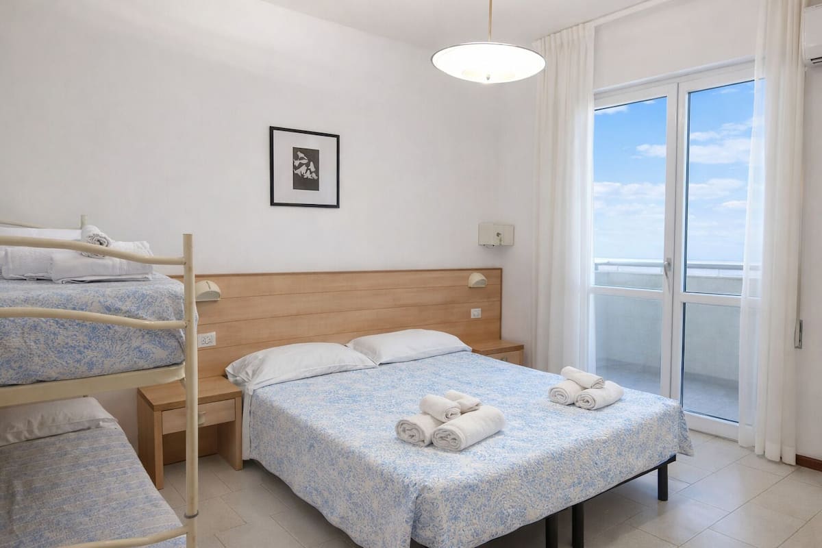 Hotellihuone, jossa on sänky, kerrossänky, yöpöytä, ikkuna, josta on näkymä, ja kattovalaisin.