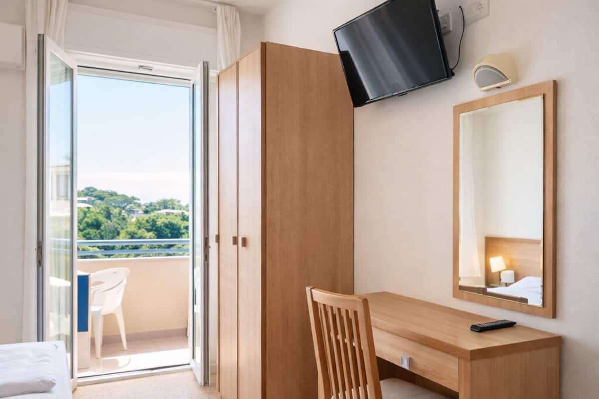 Hotellihuone, jossa on sänky, työpöytä, tuoli, televisio, peili ja parveke, jolta on näkymä.
