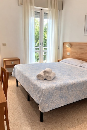 Une chambre à coucher avec un lit, une table de chevet, une tête de lit en bois et une vue sur l’extérieur, visible à travers une porte vitrée.
