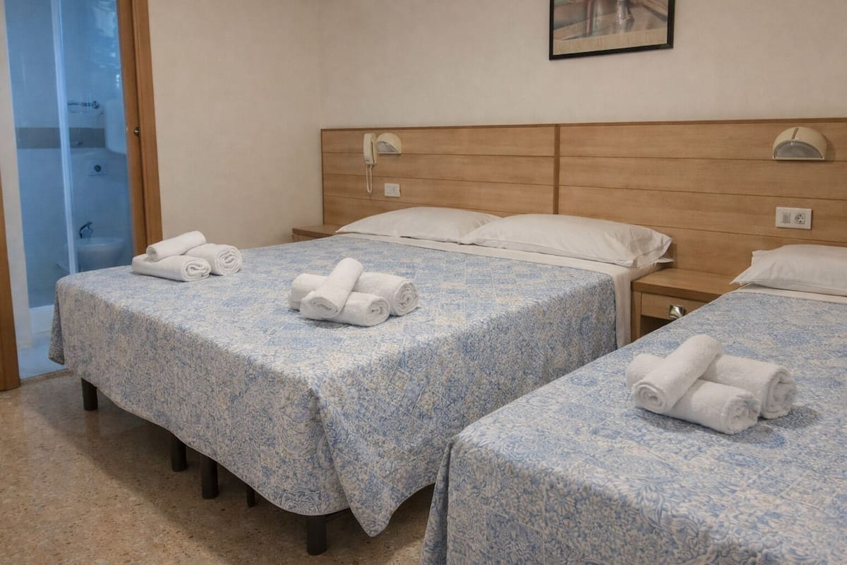 Hotellihuone, jossa on kaksi sänkyä, ja jokaisessa sängyssä on kuviollinen peitto ja rullalle taitetut pyyhkeet.