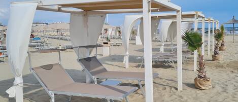 A beach with white sunbeds and umbrellas, some potted plants, and a clear sky.