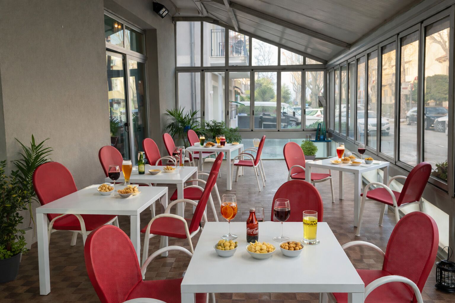 An outdoor dining area with tables and chairs, food and drinks, and large windows.