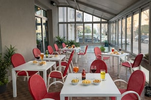 Un espace de restauration en plein air, avec des tables et des chaises, de la nourriture et des boissons, ainsi que de grandes fenêtres.