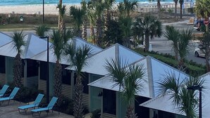 Blick auf einen Strand mit einer Mole, Palmen und Liegestühlen.