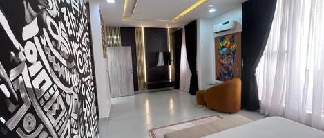 A modern hotel room with a large bed, a wall with abstract art, a painting, and a large window with curtains.