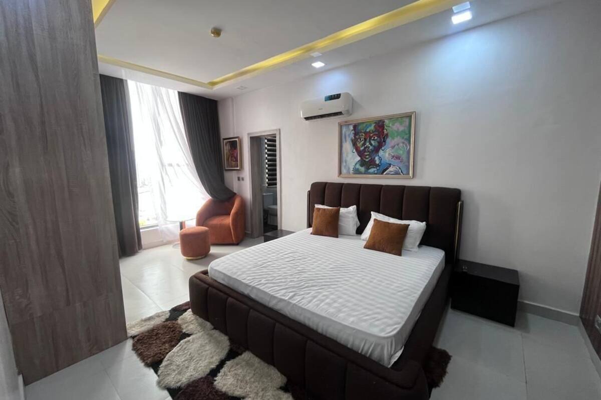 A bedroom with a large bed, a chair, a painting, and a window.