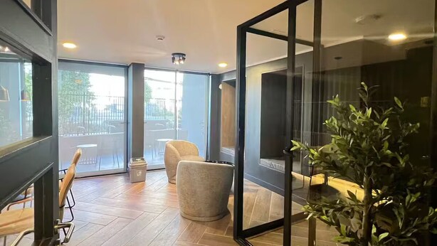 Quarto de hotel moderno com uma grande porta de vidro deslizante que dá para uma área externa, piso de madeira, um espelho grande e um vaso com planta.