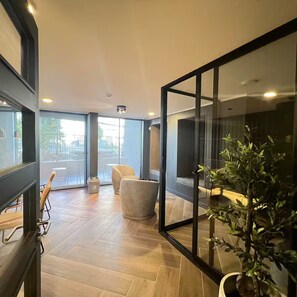 A modern hotel room with a large sliding glass door leading to an outdoor area, a wooden floor, a large mirror, and a potted plant. - Patagonia Lounge - Lluvia (La Florida)