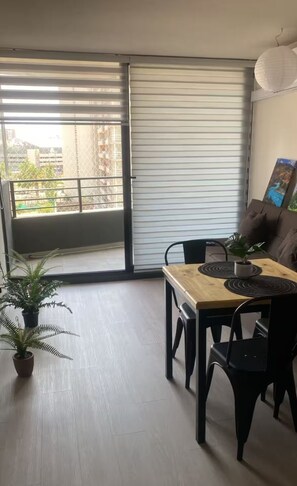 A dining area with a wooden table, black chairs, a potted fern, and a sliding glass door leading to a balcony. - Patagonia Lounge - Lluvia (La Florida)