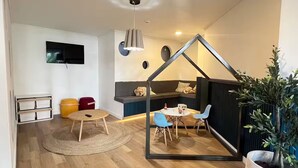 Uma sala de estar moderna com piso de madeira, uma TV na parede, um sofá, uma mesa de jantar com cadeiras e um lustre.