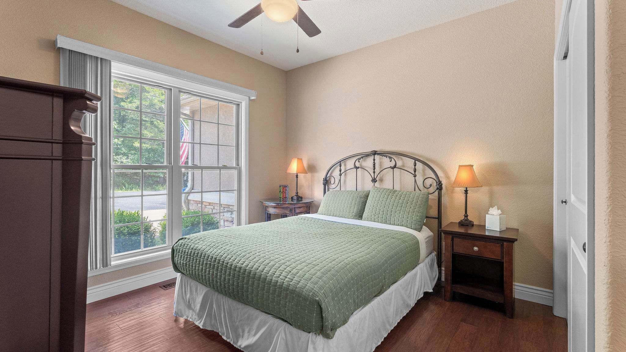 A bedroom with a bed, two bedside tables, a ceiling fan, and a large window.