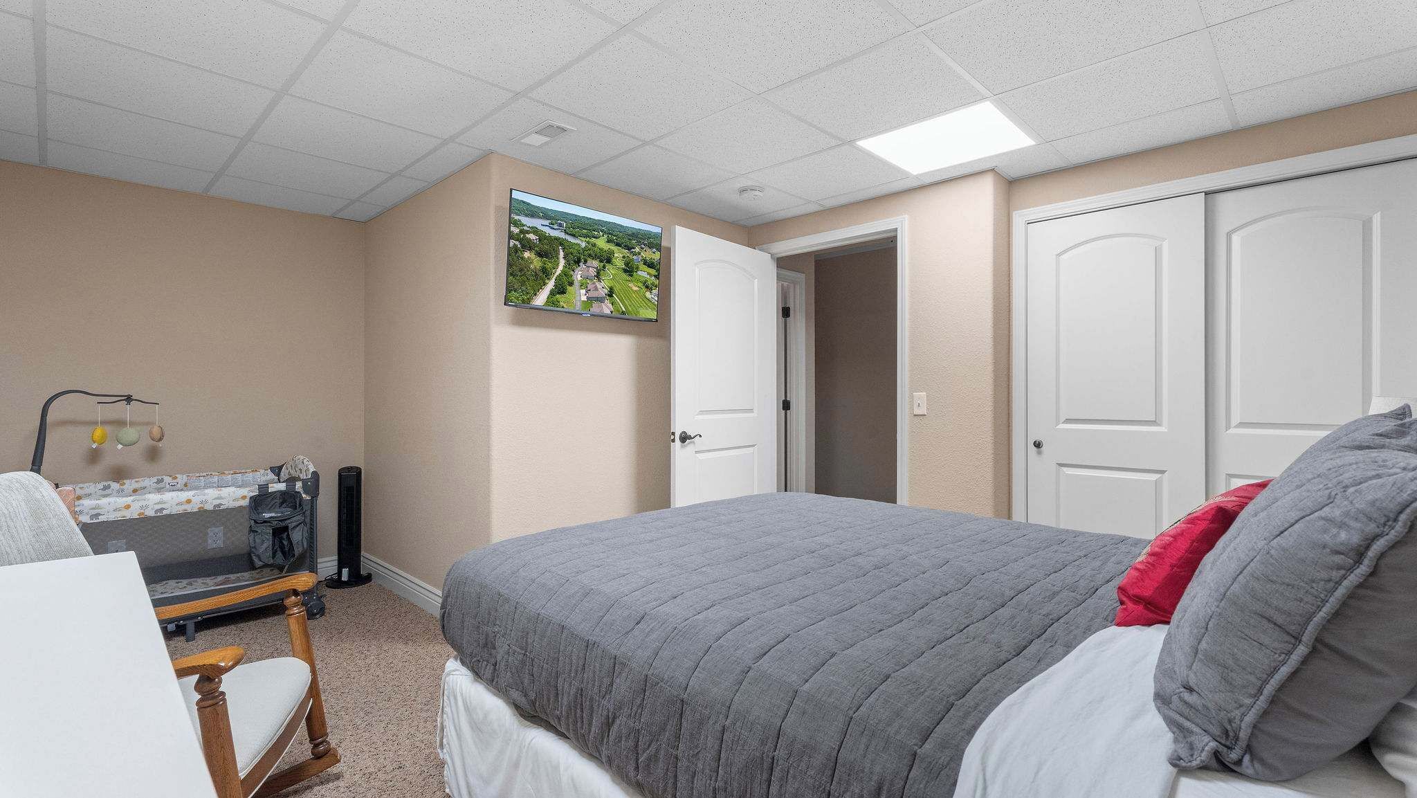 A bedroom with a bed, a desk with a chair, a TV on the wall, and a door.
