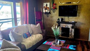 A cozy living room with a sofa, a fireplace, a TV, and a window with curtains. - Mountain views, quiet location, Close to Fort Sill and Medicine Park! (Lawton)
