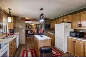 A compact kitchen with wooden cabinets, a white refrigerator, a microwave, and a small island with a sink.