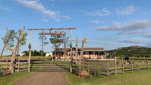 A rustic wooden archway labeled "Bunkhouse" leading to a building with a covered porch and a fenced pasture in the background. - Mountain views, quiet location, Close to Fort Sill and Medicine Park! (Lawton)