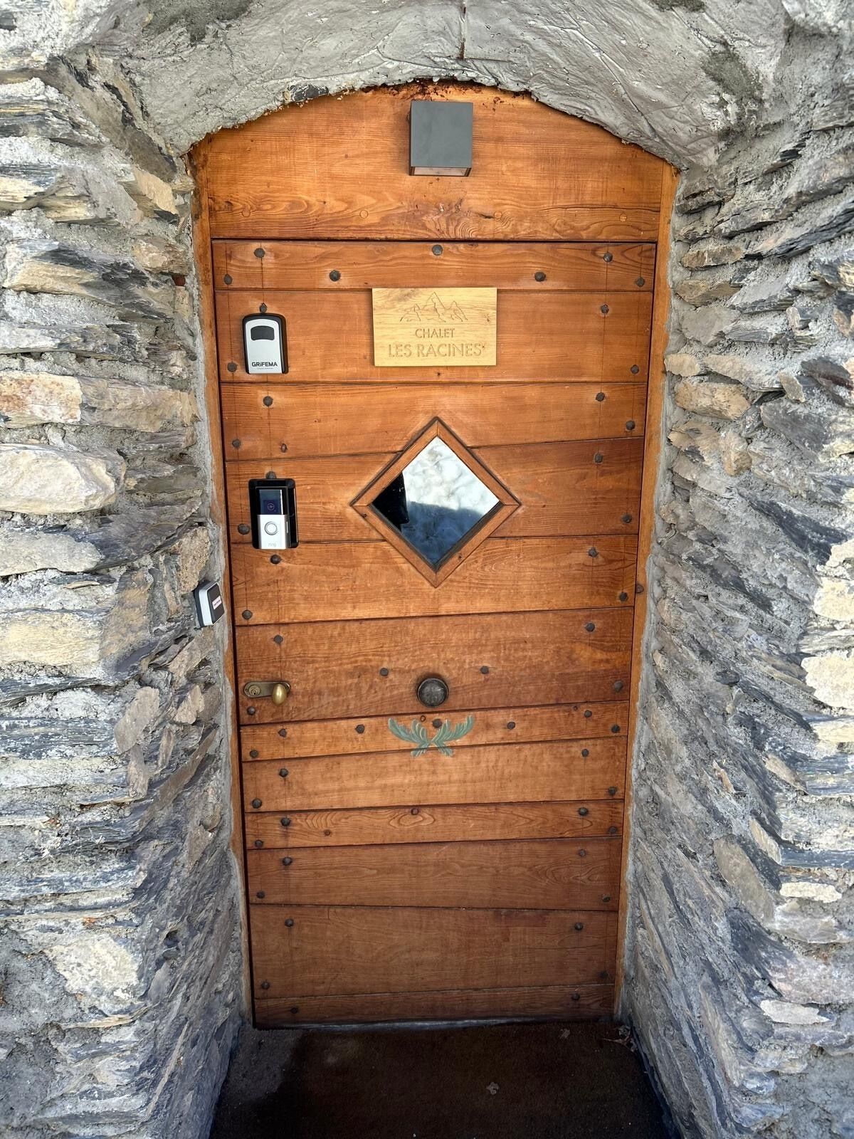 A wooden door with a plaque reading "Chalet Les Racines" and a small window.