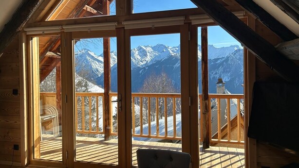 Een houten chalet met grote ramen en uitzicht op de bergen.