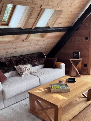 A cozy attic room with a wooden ceiling, a sofa, a coffee table, and a guest book. - Chalet Les Racines (Villard-Reculas)