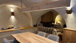 Een gezellig eetgedeelte met een houten tafel en grijs gestoffeerde stoelen, een keuken achtergrond en een houten plafondconstructie.