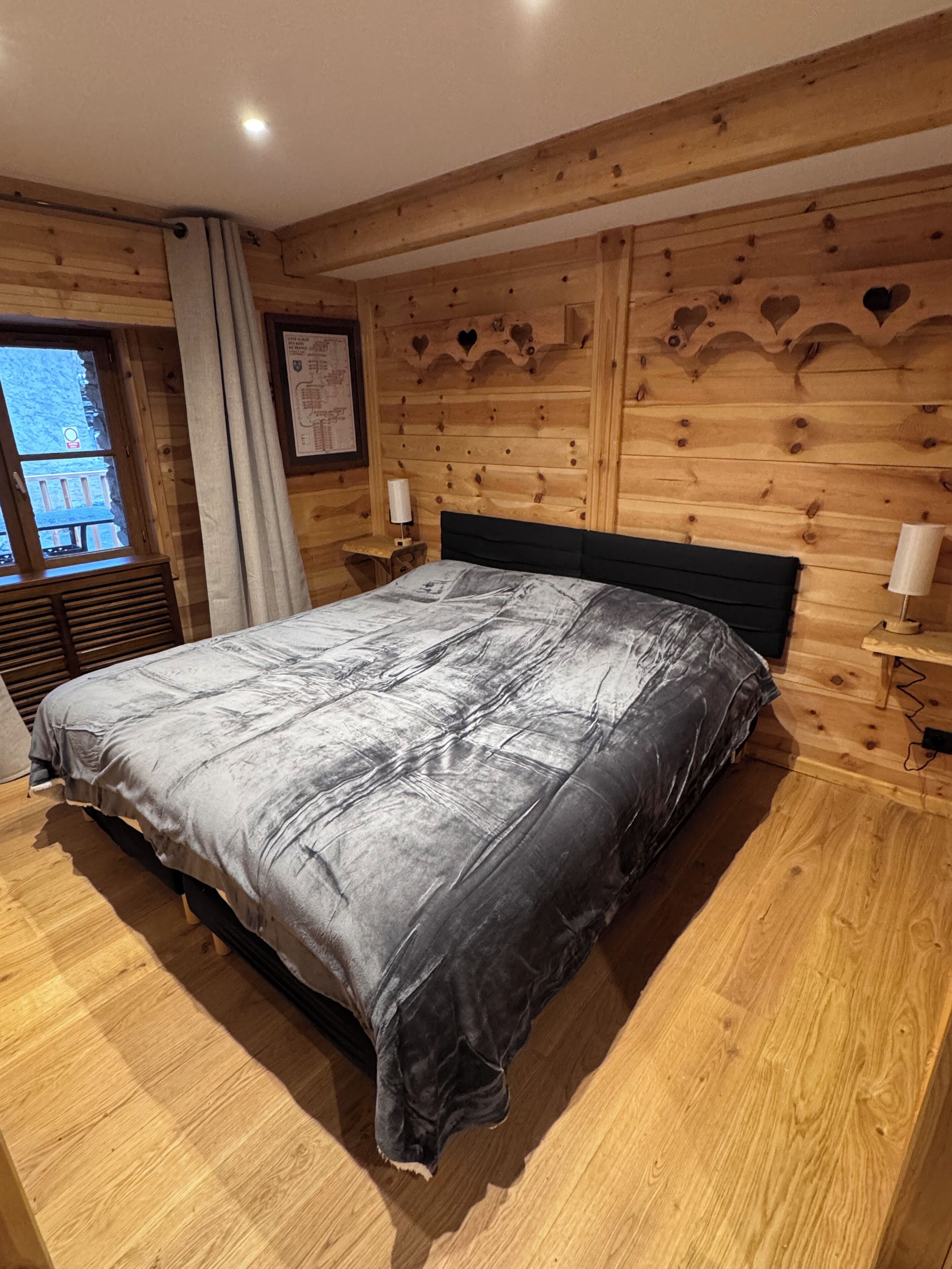 A wooden-paneled bedroom with a bed, a window, and a wall-mounted lamp.